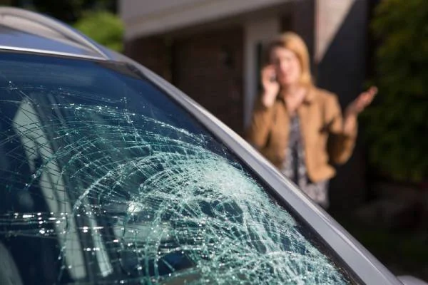 Shattered car windshield with a woman standing behind it.