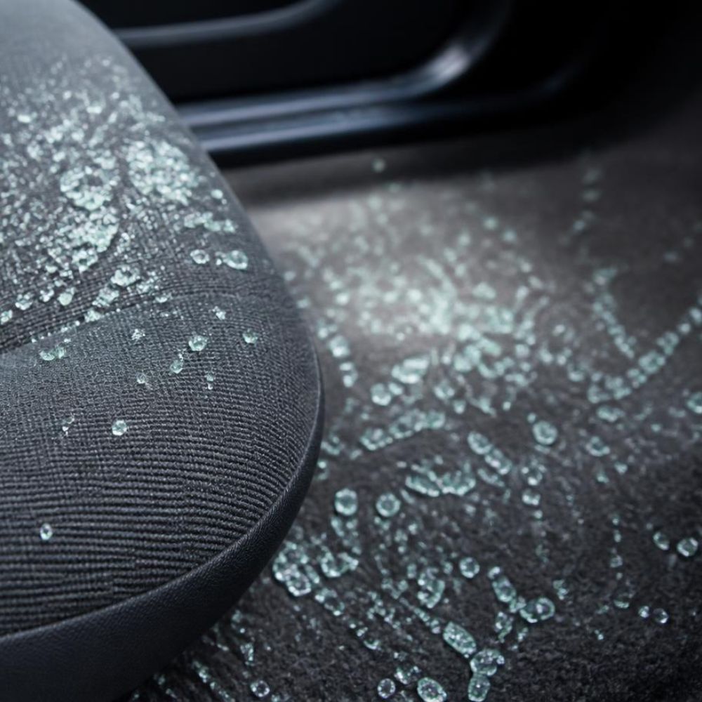 Shattered tempered glass pieces scattered across a car seat and floor after a side window break