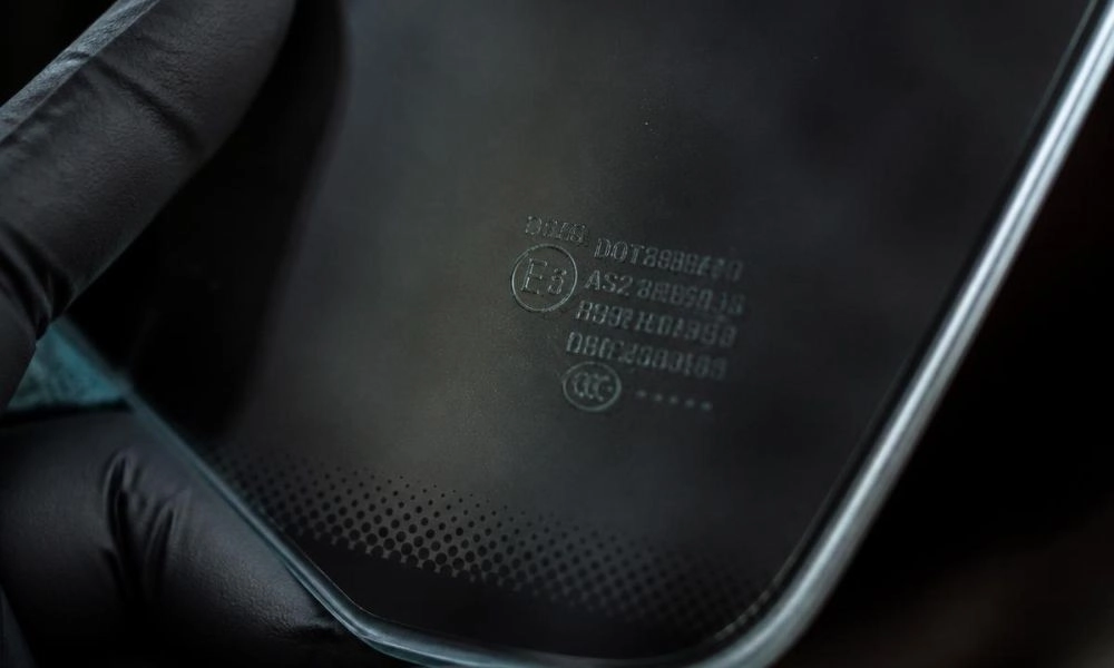Technician holding car glass showing the DOT code stamp and certification markings