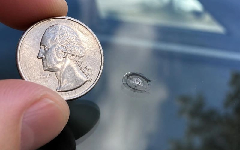 Quarter coin held up to compare the size of a small windshield chip before repair in Charlotte